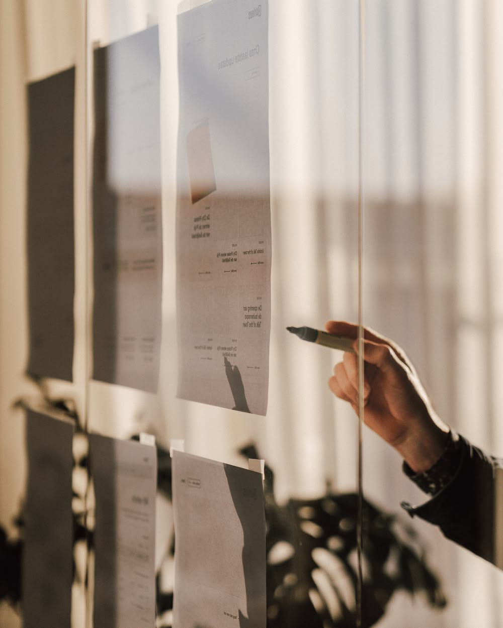 Une main annote au marqueur des feuilles affichées sur une vitre
